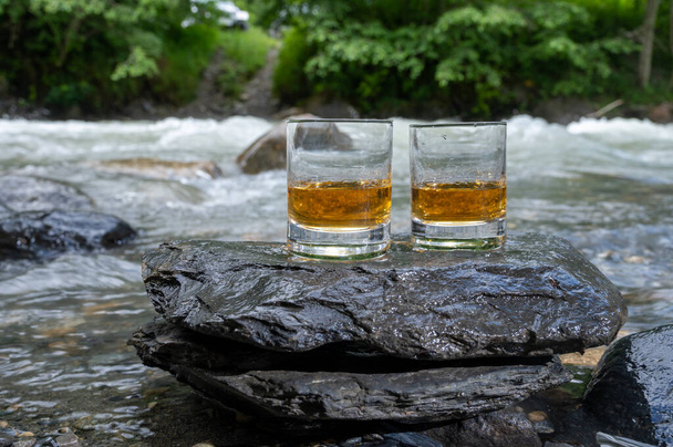 Ποτήρι από ισχυρό ουίσκι single malt ουίσκι με γρήγορη ροή ποτάμι βουνό στο παρασκήνιο, Σκωτία - Φωτογραφία, εικόνα