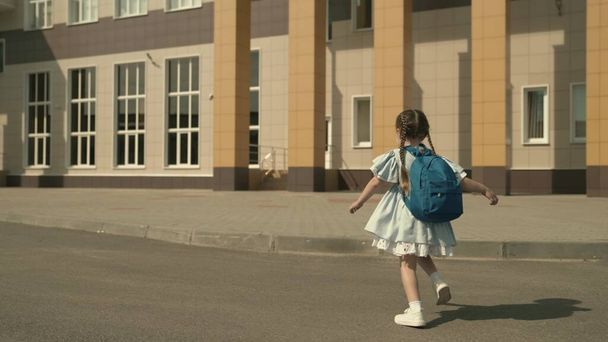 Начальная школа ребенок бегает по школьному двору с рюкзаком на плечах, маленький ребенок первоклассник, современная учебная программа, активный ребенок на улице, желание быть умной, счастливой девушкой - Фото, изображение