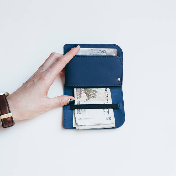 A lány kék karcsú modern táskát tart a hitelkártyákhoz és bankjegyekhez. A lány kék karcsú modern táskát tart a hitelkártyákhoz és bankjegyekhez. Stílusos minimalista kiegészítők ökobőrből. Lapos feküdt közel fénykép. - Fotó, kép