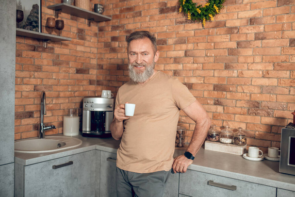 A midagedman standing in the kitchen with a coffee cup in hands - Valokuva, kuva