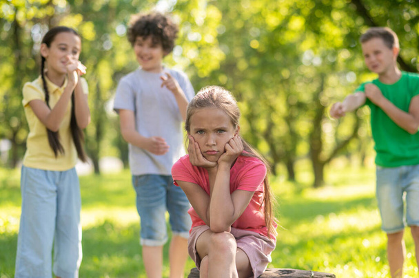 Sad girl and kids mocking behind outdoors - Foto, imagen
