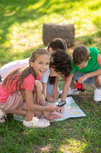 Enthusiastic girl with magnifying glass and friends with map - Foto, Imagem