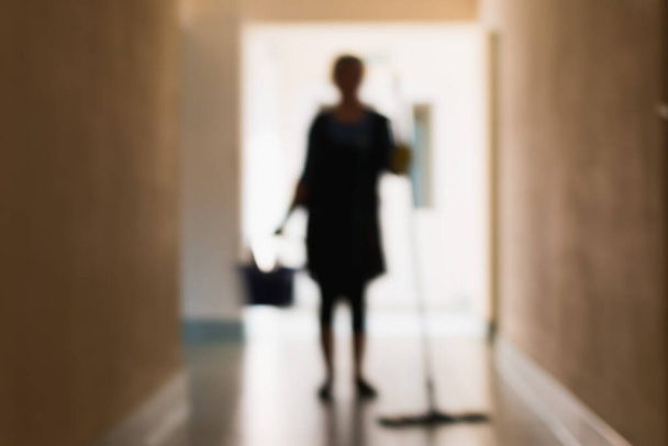 A blurry image of a woman cleaning the premises during the cleaning of the corridor and office - Foto, immagini