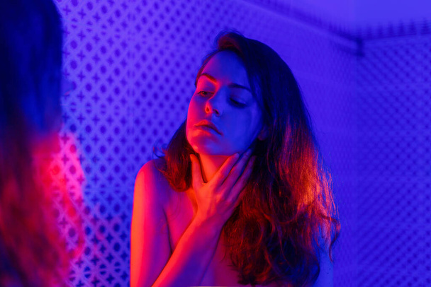 Tired young woman in depression holds choke neck with her hand in bathroom before suicide. Concept of mental Psychological health depression Panic attack . Neon Blue and red light Mirror reflection  - Foto, Bild
