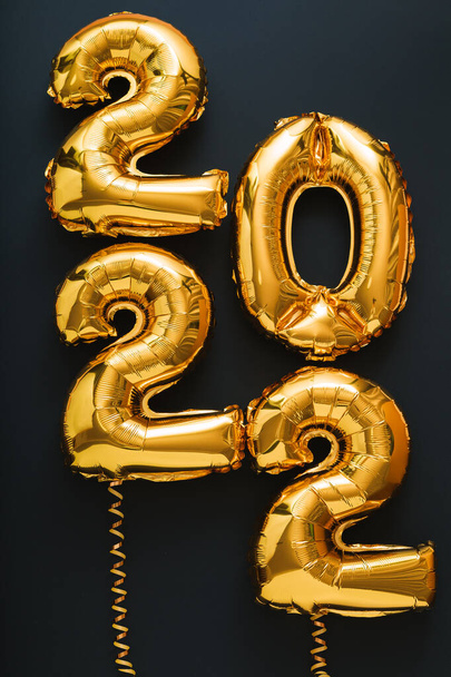 2022 év arany lufi fekete háttér arany szalagokkal. Boldog Új Évet meghívó karácsonyi arany fólia léggömbök 2022 szöveg függőleges ajándék kártya - Fotó, kép