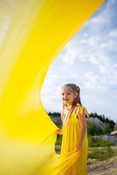 Mädchen im gelben Kleid mit Flügeln in einem gelben Tuch in der Nähe des Sees - Foto, Bild