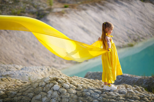 Mädchen im gelben Kleid mit Flügeln in einem gelben Tuch in der Nähe des Sees - Foto, Bild