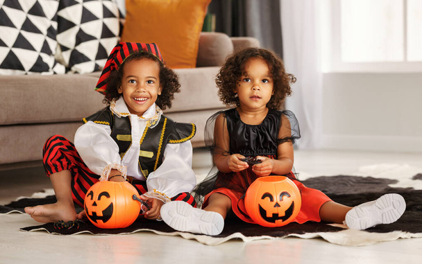 Due simpatici bambini africani americani fratello e sorella in costumi di Halloween che giocano insieme sul pavimento a casa - Foto, immagini