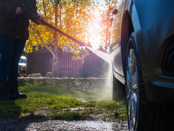 het meisje wast de auto thuis bij de garage met behulp van een hogedrukreiniger - Foto, afbeelding