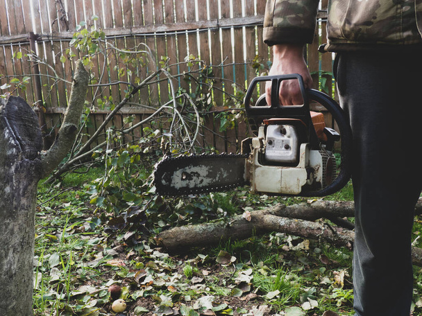Um homem segura uma motosserra profissional em suas mãos, ele está pronto para serrar árvores no jardim - Foto, Imagem