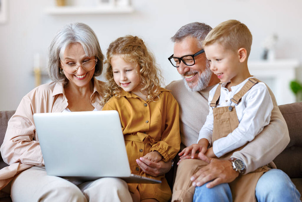 Smiling senior grandparents and cute little grandchildren watching cartoons on laptop - Fotografie, Obrázek