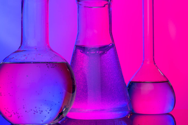 Chemical glassware close up on neon pink-purple background - Foto, Imagen