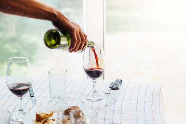 ガラスにワインを注ぐ男の手。バーベキューと日曜日のランチタイムにアルゼンチンの家族のテーブル. - 写真・画像
