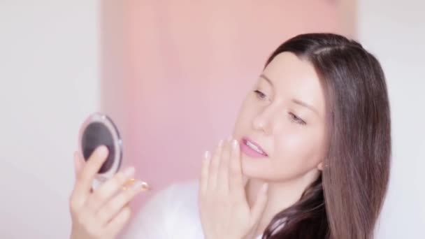 Woman looking at compact mirror and examines her skin, touching face and smiling, long hairstyle and natural makeup, beauty face portrait of female model as cosmetic product and skincare commercial - Footage, Video