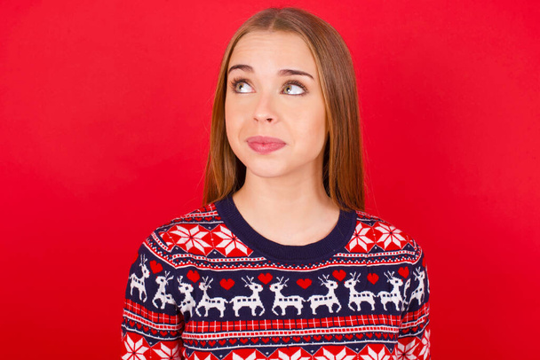 молода біла дівчина в різдвяному светрі дивиться в сторону порожнього простору вдумлива
 - Фото, зображення