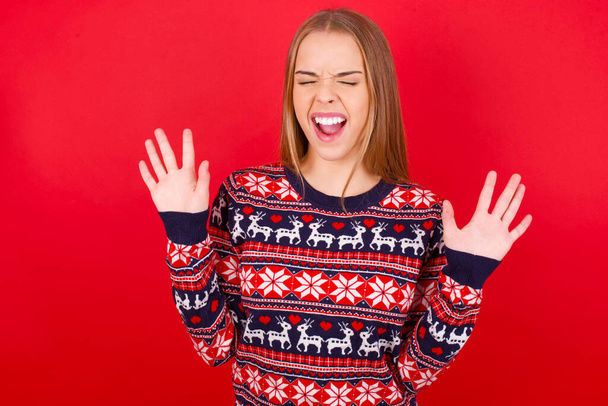 Emotivo joven caucásica chica usando navidad suéter se ríe en voz alta, oye broma divertida o historia, levanta las palmas con satisfacción, siendo muy alegre divertido por amigo - Foto, imagen