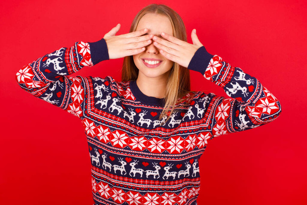 nuori valkoihoinen tyttö yllään joulu pusero peittää silmät kädet hymyillen iloinen ja hauska. Sokea käsite. - Valokuva, kuva