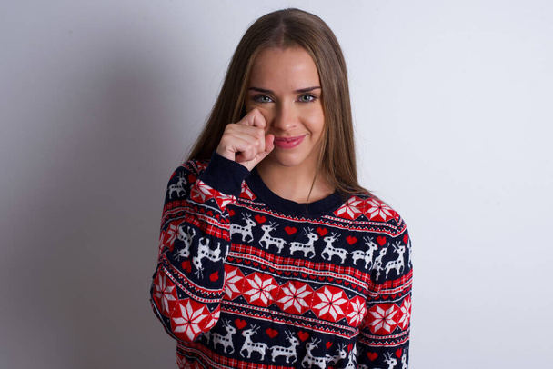 Csalódott depressziós fiatal kaukázusi lány visel karácsonyi pulóver fehér háttér törlőkendő könnyek áll stresszes kifejezés. Negatív érzelem - Fotó, kép