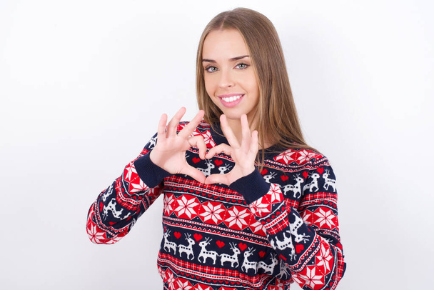 Beyaz arka planda Noel süveteri giyen Kafkasyalı kız ellerini çapraz tutuyor düşünceli bir şekilde duruyor. - Fotoğraf, Görsel