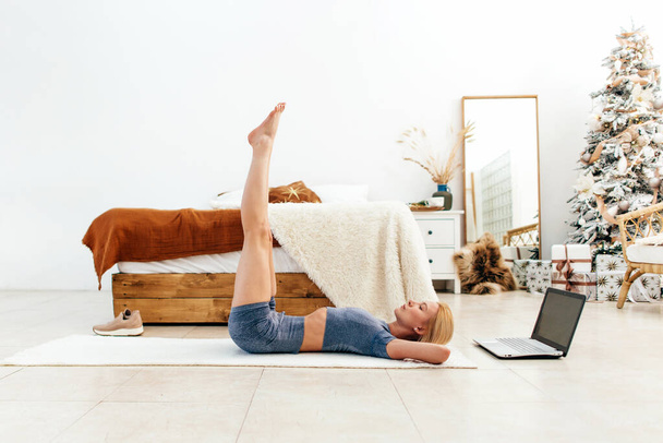 Mujer entrenando los músculos abdominales levantando las piernas tumbadas en el suelo - Foto, Imagen