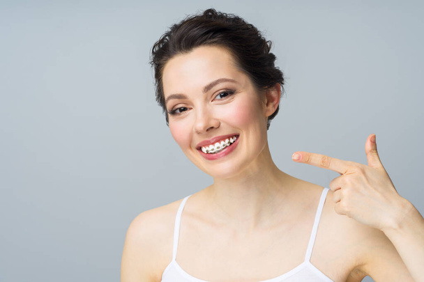 Une jeune femme avec des bretelles sur les dents, sourit et pointe vers l'espace de copie avec un geste de la main - Photo, image