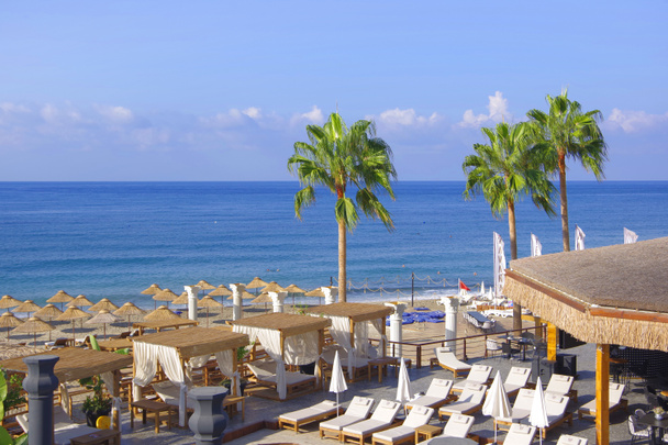 Blick auf den Strand am Mittelmeer. Sonnenschirme und Liegestühle warten auf die Urlauber. - Foto, Bild