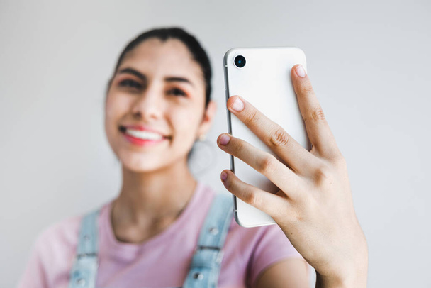 Jeune femme latine prendre selfie des mains téléphone sur fond gris en Amérique latine - Photo, image
