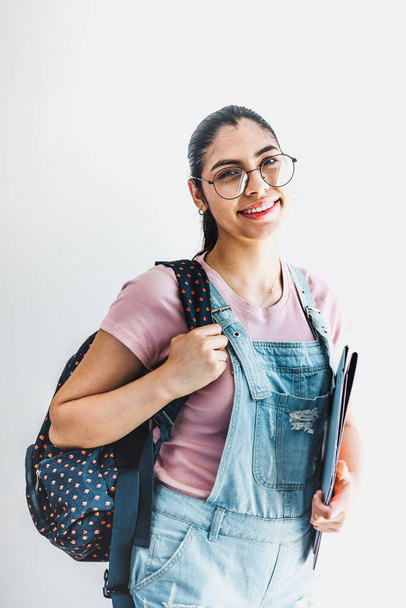Giovane studentessa latina in possesso di quaderni ridere con gli occhiali su sfondo grigio isolato in America Latina - Foto, immagini