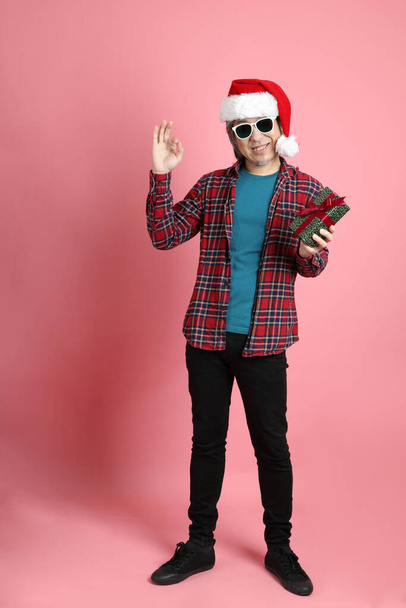 The senior Asian man with Christmas hat standing on the pink background. - Φωτογραφία, εικόνα