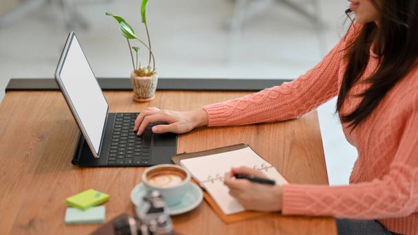 Вид сбоку молодой женщины, работающей, печатающей на беспроводной цифровой планшет с клавиатурой во время проверки списка в своем дневнике в офисе. - Фото, изображение