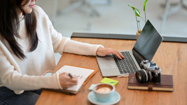 Vágott kép, Millenniumi női szabadúszó web blogger írja az online témák listáját könyvében, miközben dolgozik laptop kávézóban. - Fotó, kép