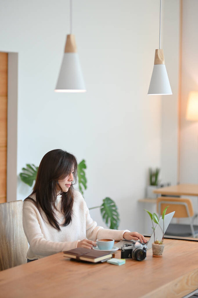 Чарівна молода азіатська жіноча кав'ярня або туристичний блогер, що працює на її ноутбуці в сучасному стильному кафе
 - Фото, зображення