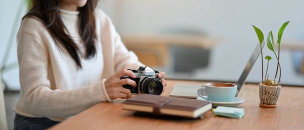Przycięte zdjęcie samicy freelancera z retro rocznika aparat fotograficzny, laptop i jej rzeczy na stole w kawiarni - Zdjęcie, obraz