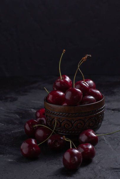 Organic juicy cherry in a bowl on dark background. Close-up photo, low key - Foto, afbeelding