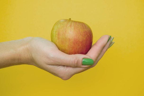 egy alma a nő tenyerében. egy lány egy vörös almát tart a kezében sárga alapon - Fotó, kép
