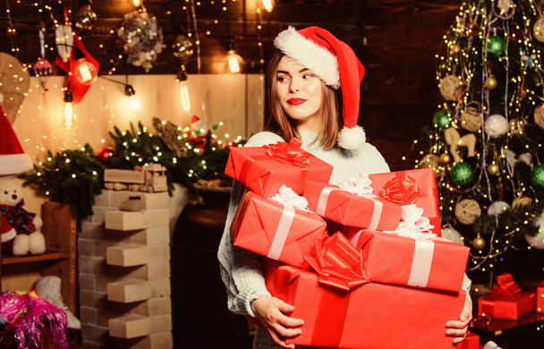 Girl stylish makeup red lips hold many christmas gifts. Cozy christmas atmosphere. Woman santa claus hat on christmas eve. Bring magic into someone elses life. Lady santa celebrate christmas at home - Фото, зображення