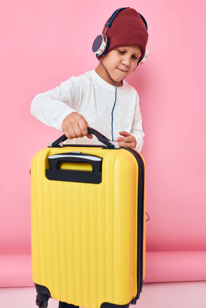 κομψό αγόρι με κίτρινη βαλίτσα φορώντας ακουστικά ψυχαγωγίας - Φωτογραφία, εικόνα