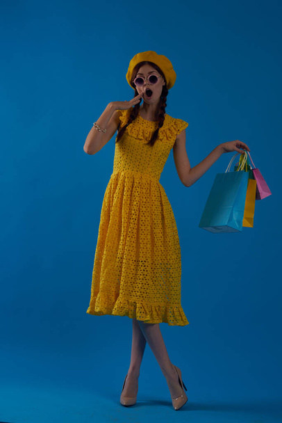 femme souriante dans un chapeau jaune style mode Shopaholic fond bleu - Photo, image