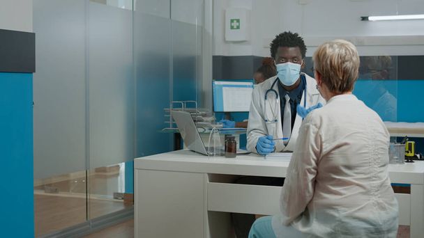 Jonge arts draagt gezichtsmasker tijdens het raadplegen van oudere patiënt - Foto, afbeelding