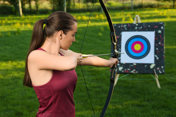 Woman with bow and arrow aiming at archery target in park - 写真・画像