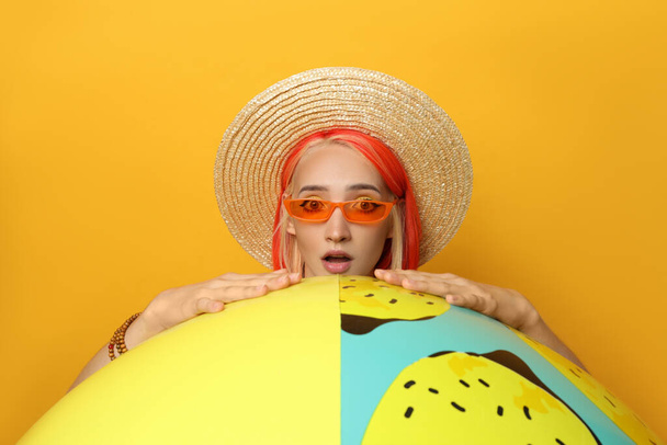Emotional young woman with bright dyed hair and inflatable ball on orange background - Foto, Bild