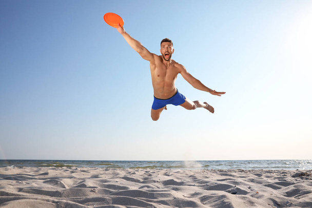 Sportive man jumping and catching flying disk at beach - Photo, Image