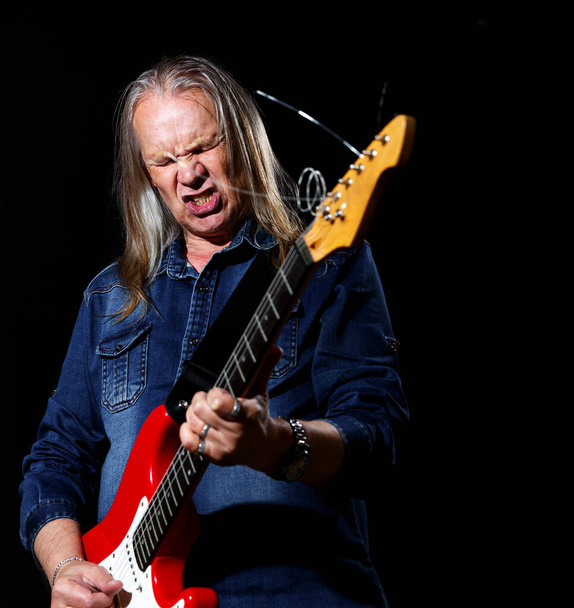elderly man with long gray hair in blue denim shirt plays the electric guitar on black background - Photo, Image