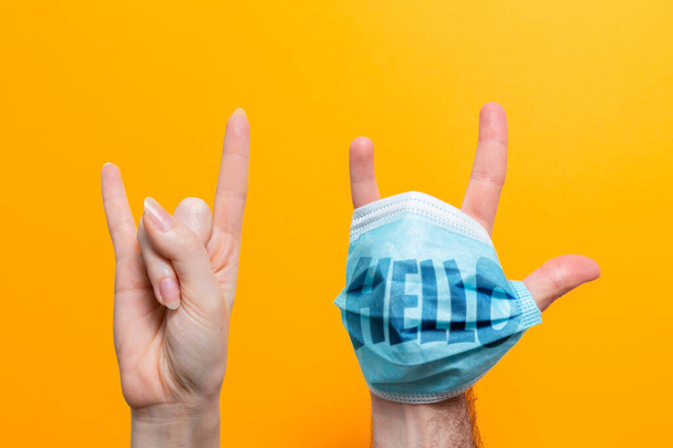 World Hello day. A female's hand and a male's hand with a mask on, fingers spread. Inscription on the mask Hello. Yellow background. The concept of protection from the virus. - Fotoğraf, Görsel