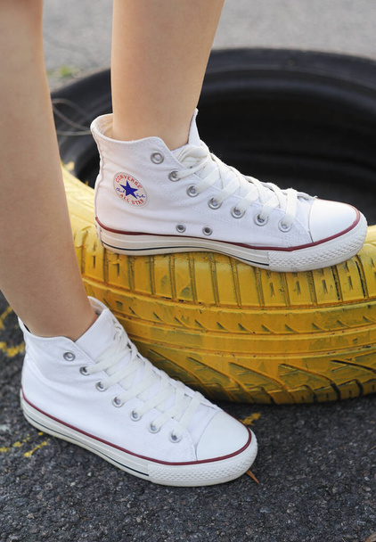Belarus, Minsk - June 27, 2019: a girl in white cloth Converse sneakers stands on old car tires. - Foto, imagen