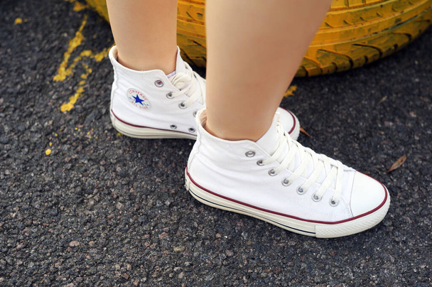 Belarus, Minsk - June 27, 2019: a girl in white cloth Converse sneakers stands on old car tires. - Foto, imagen