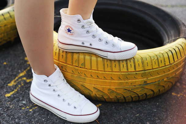 Belarus, Minsk - June 27, 2019: a girl in white cloth Converse sneakers stands on old car tires. - Foto, Imagem