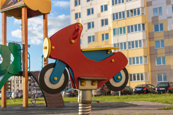 Kinderschommel in de vorm van een motorfiets. Element van de speeltuin op de binnenplaats van een appartementencomplex in een woonwijk van de stad - Foto, afbeelding
