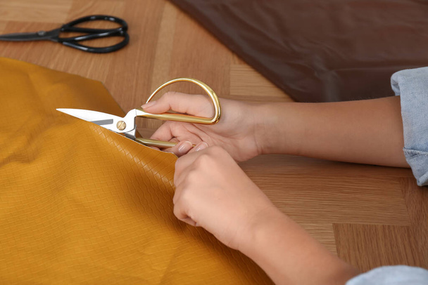 Woman cutting orange leather with scissors at wooden table, closeup - Фото, изображение