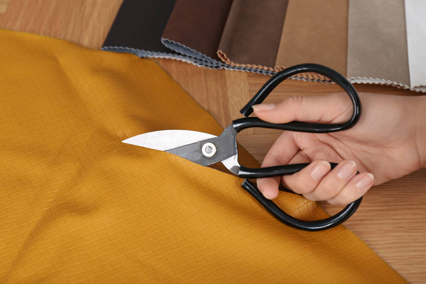 Woman cutting orange leather with scissors at wooden table, closeup - Photo, Image